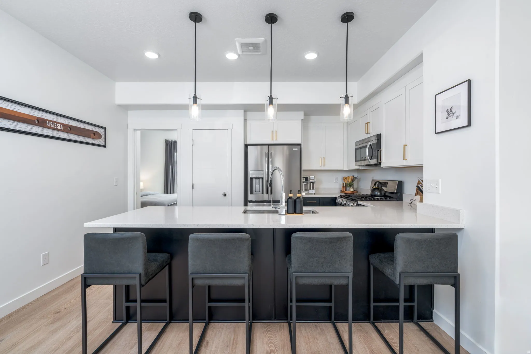 Kitchen featuring a peninsula, a breakfast bar area, stainless steel appliances, white cabinetry, and pendant lighting
