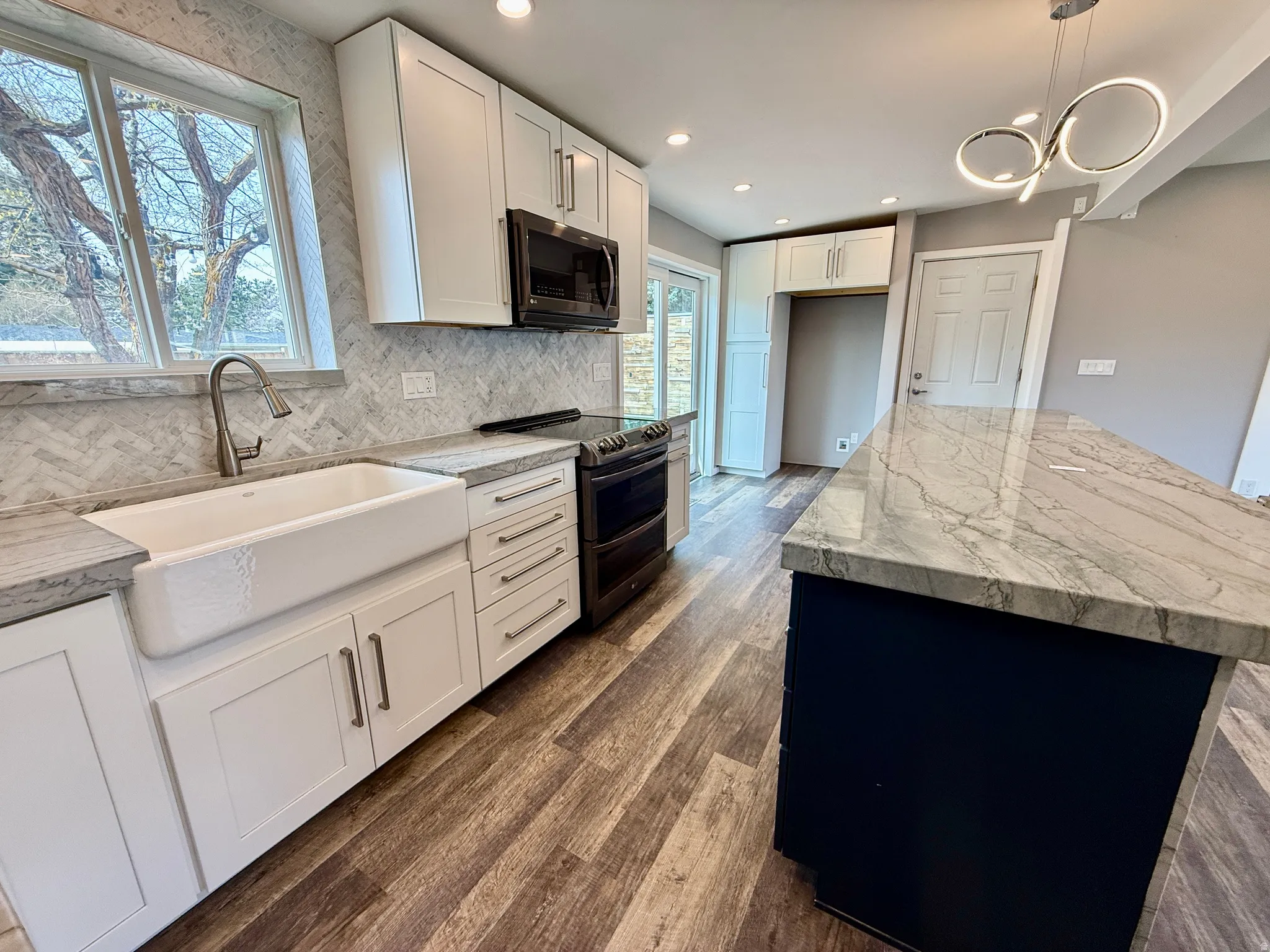 Kitchen with range with two ovens, black microwave, dark wood finished floors, a kitchen island, and decorative marble backsplash