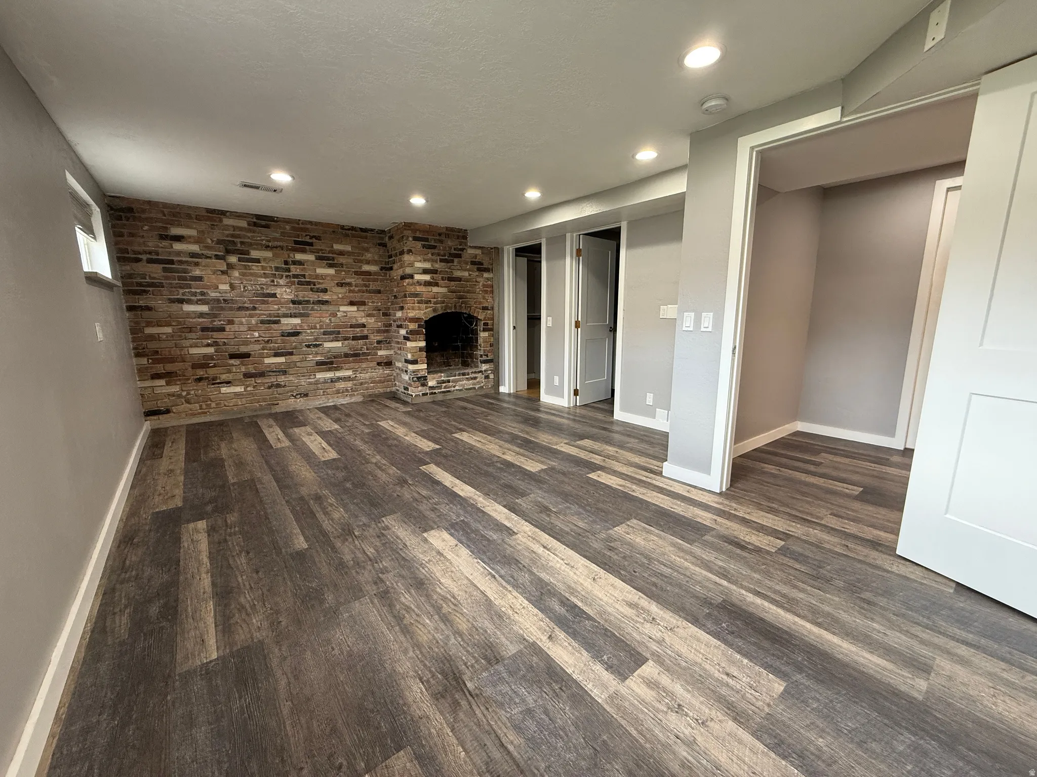 Master bedroom featuring brick wall, dark wood-type flooring, recessed lighting, and a fireplace