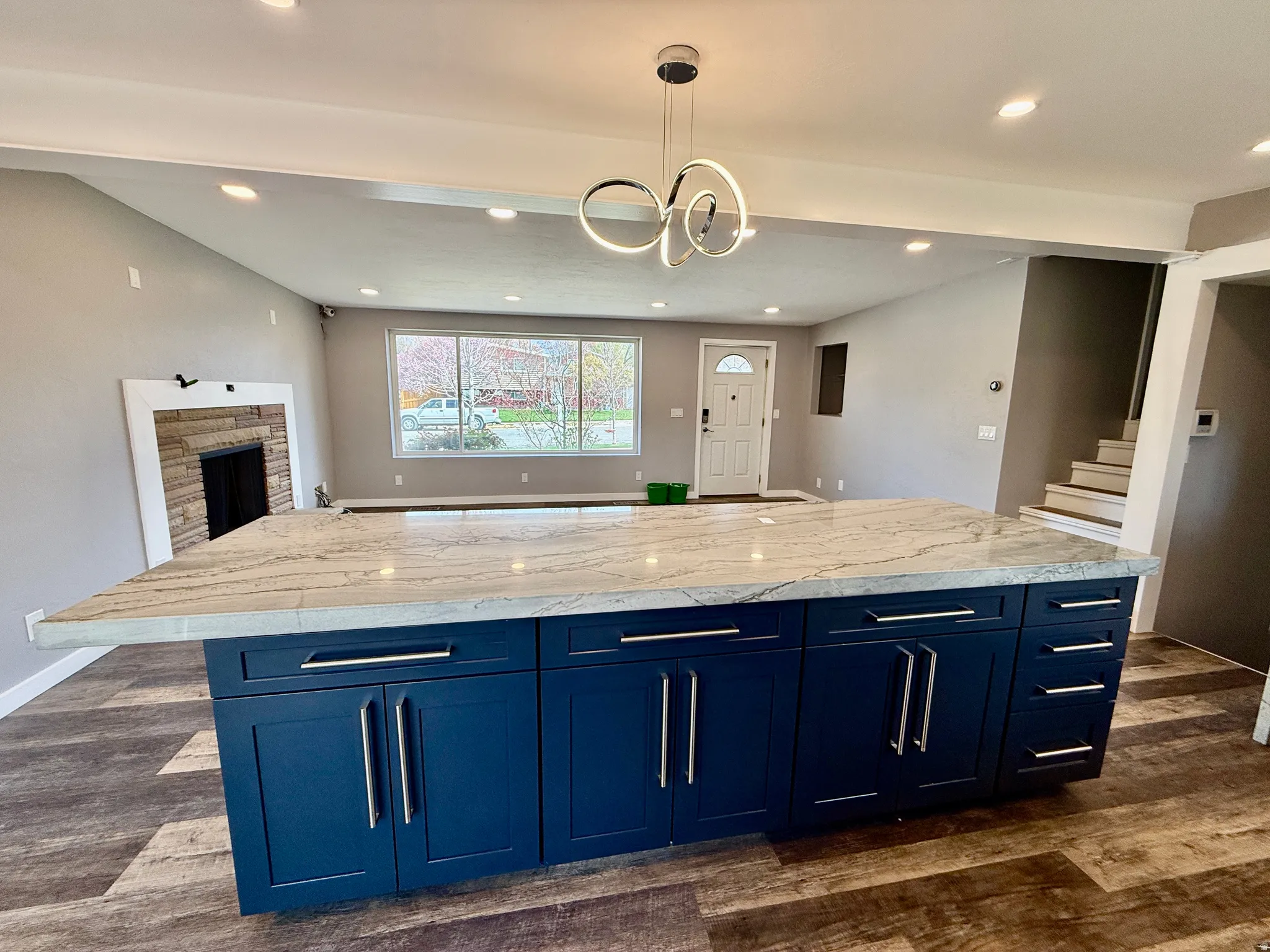 Kitchen with blue cabinetry, a spacious island, open floor plan, dark wood-style floors, and a fireplace