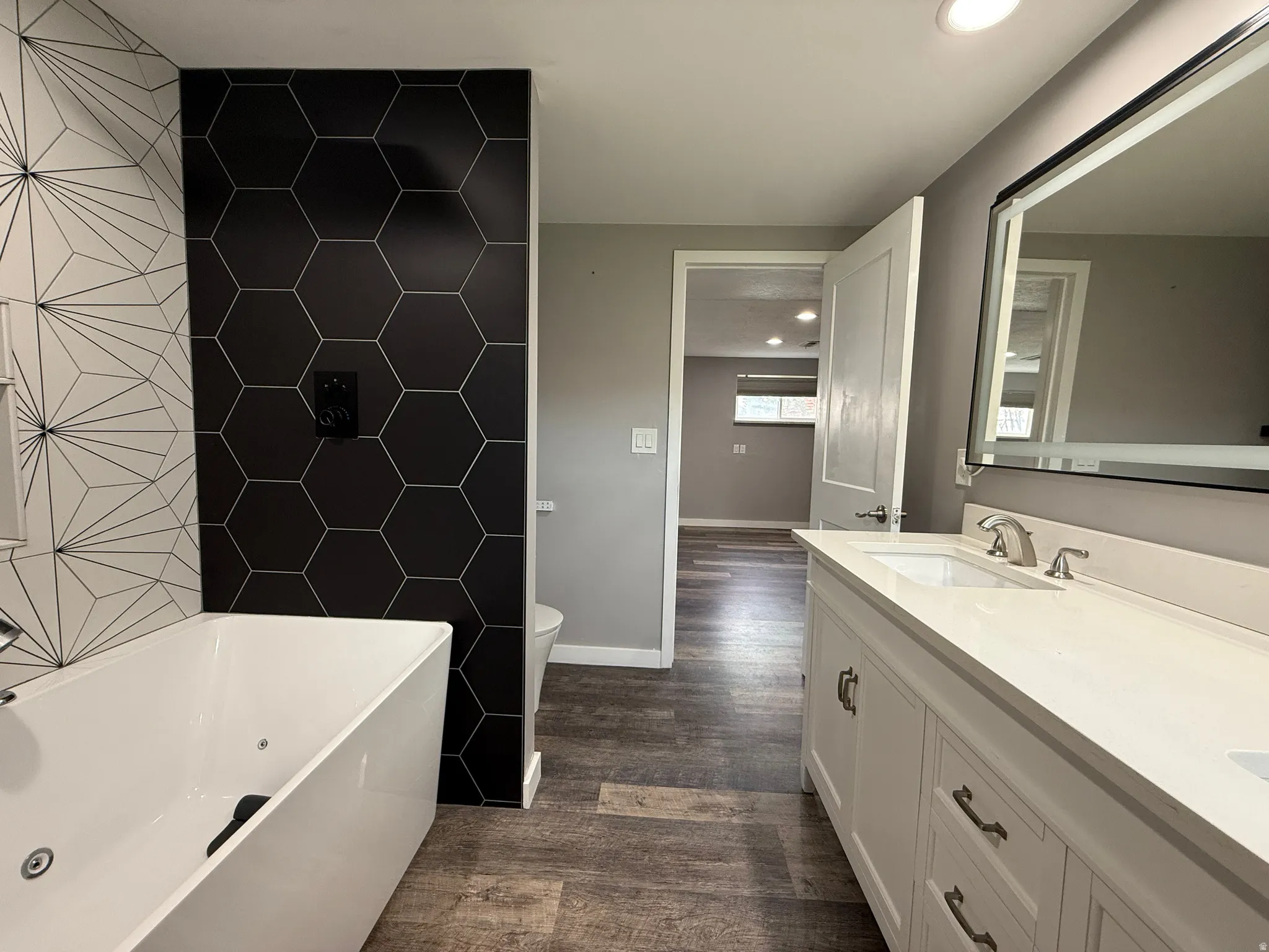 Master bedroom featuring a freestanding bath, double vanity, tile walls, dark wood finished floors, and recessed lighting
