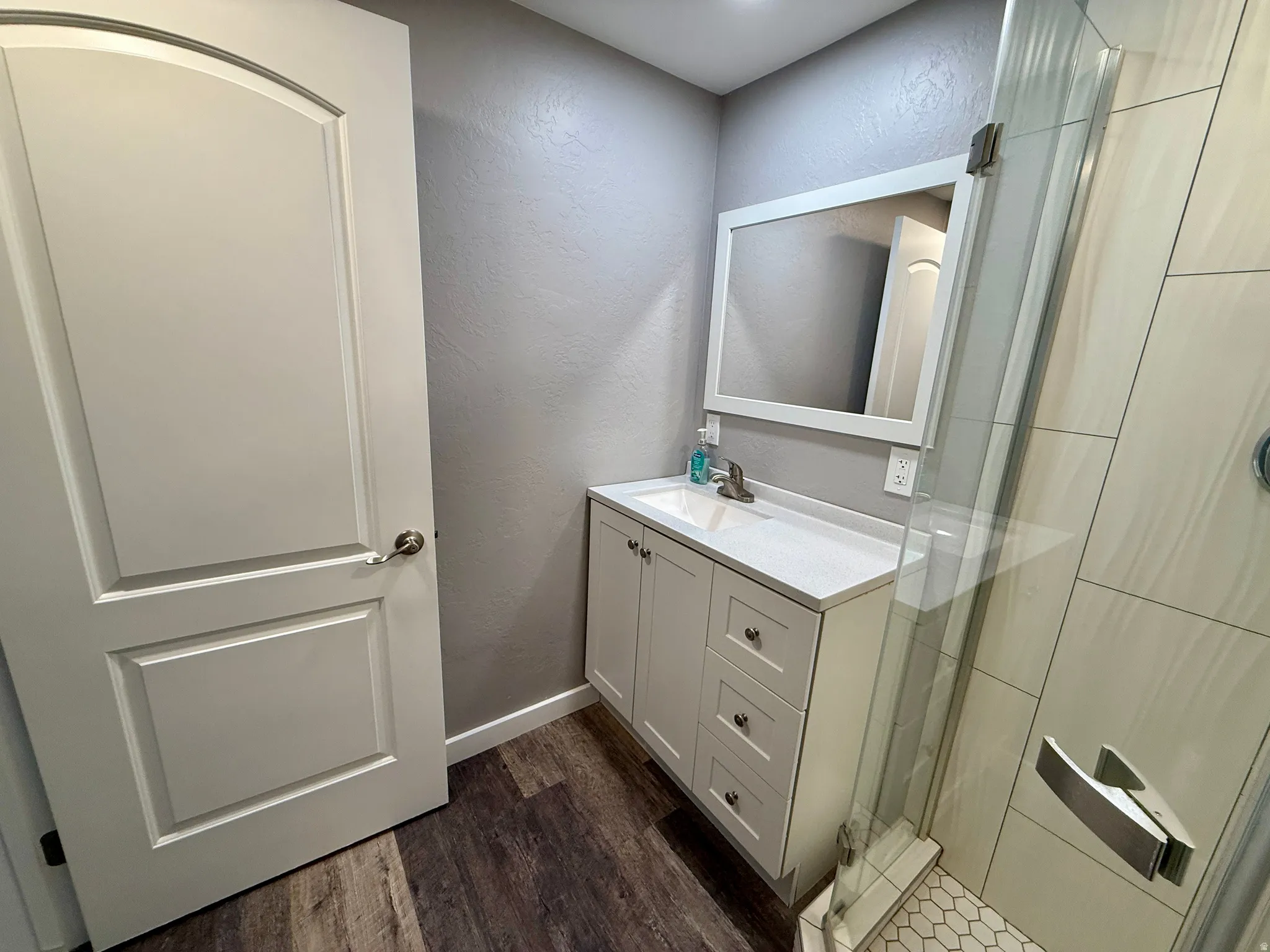 Bathroom with a textured wall, a stall shower, vanity, and dark wood-type flooring