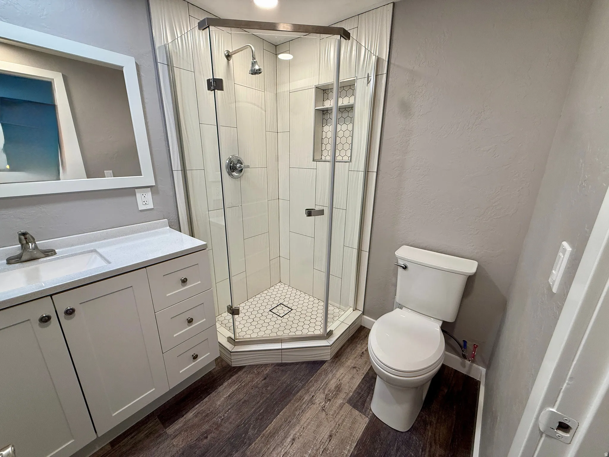 Bathroom featuring a textured wall, a stall shower, vanity, and dark wood finished floors