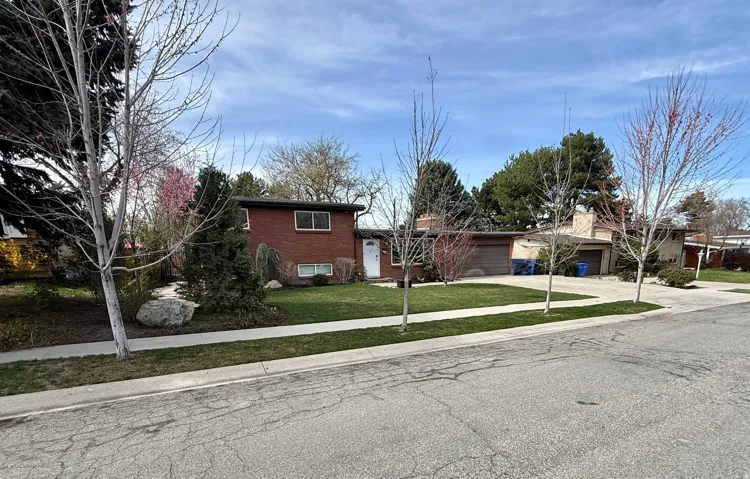 Tri-level home with driveway, brick siding, a front lawn, an attached garage, and a chimney