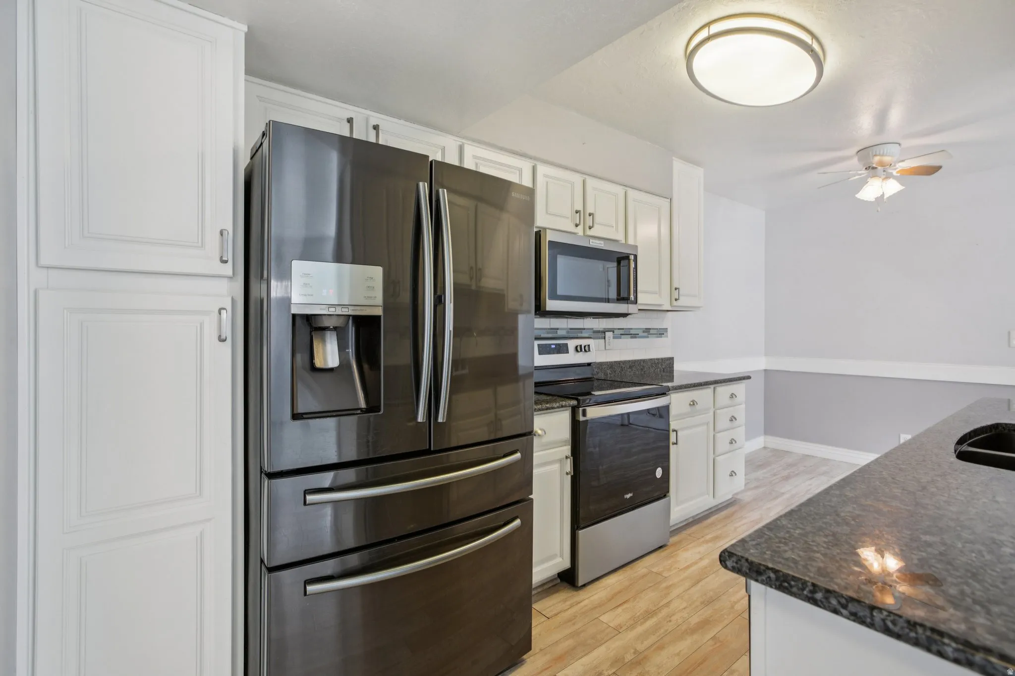Kitchen featuring stainless steel appliances, white cabinets, light wood finished floors, and a ceiling fan