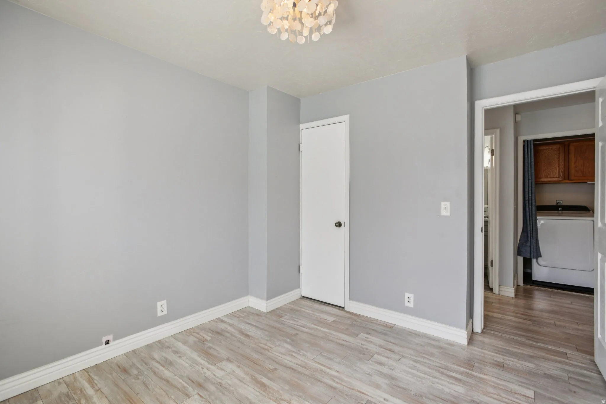 Unfurnished bedroom with washer / clothes dryer, light wood-type flooring, a chandelier, and a closet