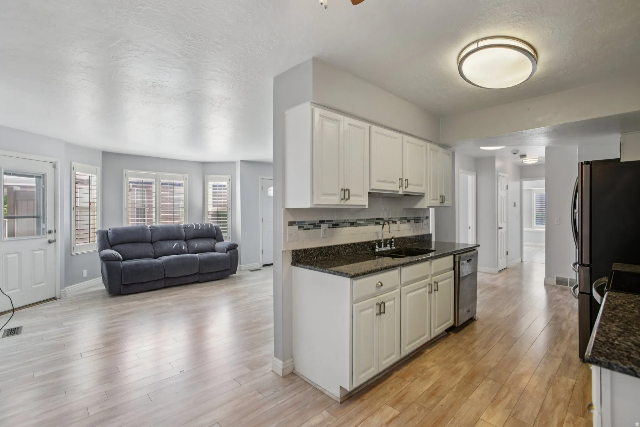 Kitchen featuring decorative backsplash, open floor plan, dark stone counters, light wood-style flooring, and white cabinets