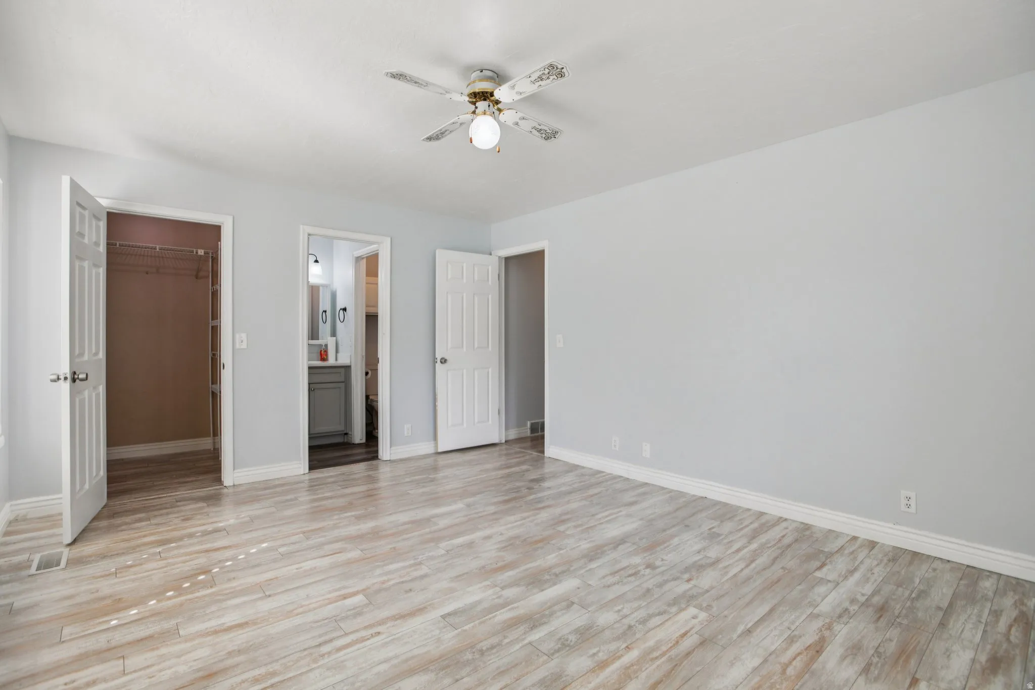 Unfurnished bedroom featuring ceiling fan, light wood-style flooring, a walk in closet, and connected bathroom