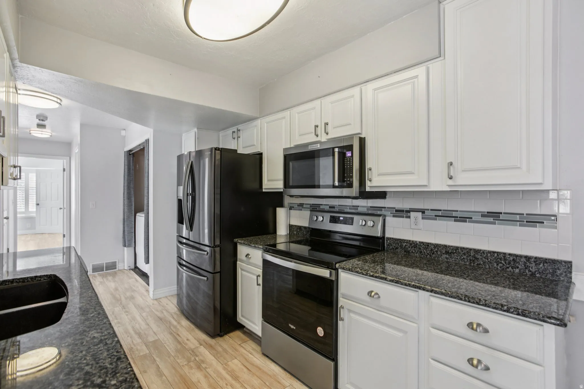 Kitchen with stainless steel appliances, white cabinetry, and dark stone counters
