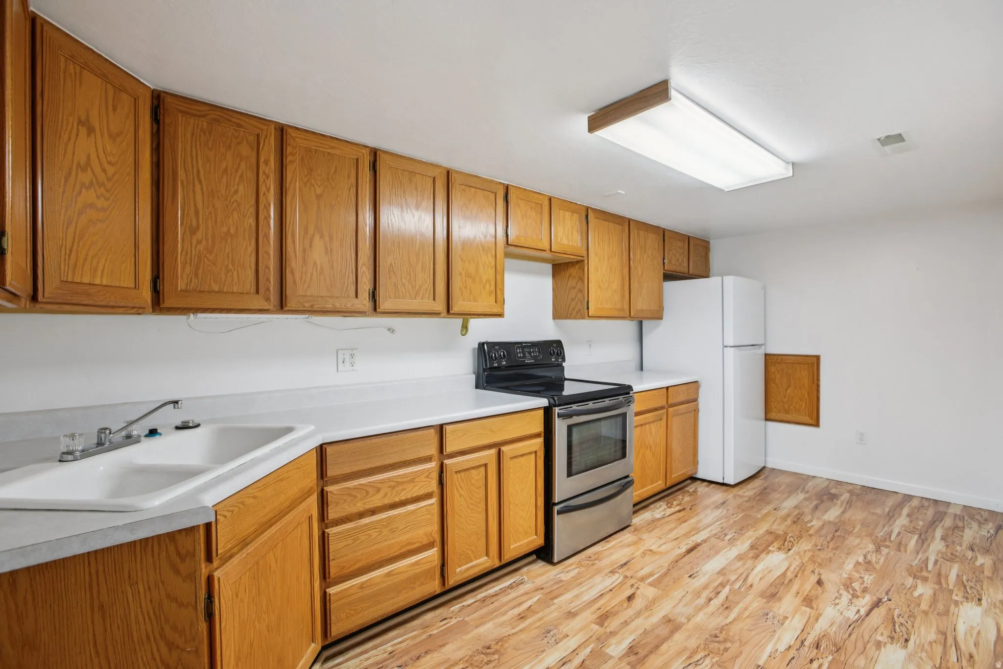 Kitchen featuring stainless steel electric range oven, freestanding refrigerator, light countertops, light wood-style floors, and wood finish cabinetry