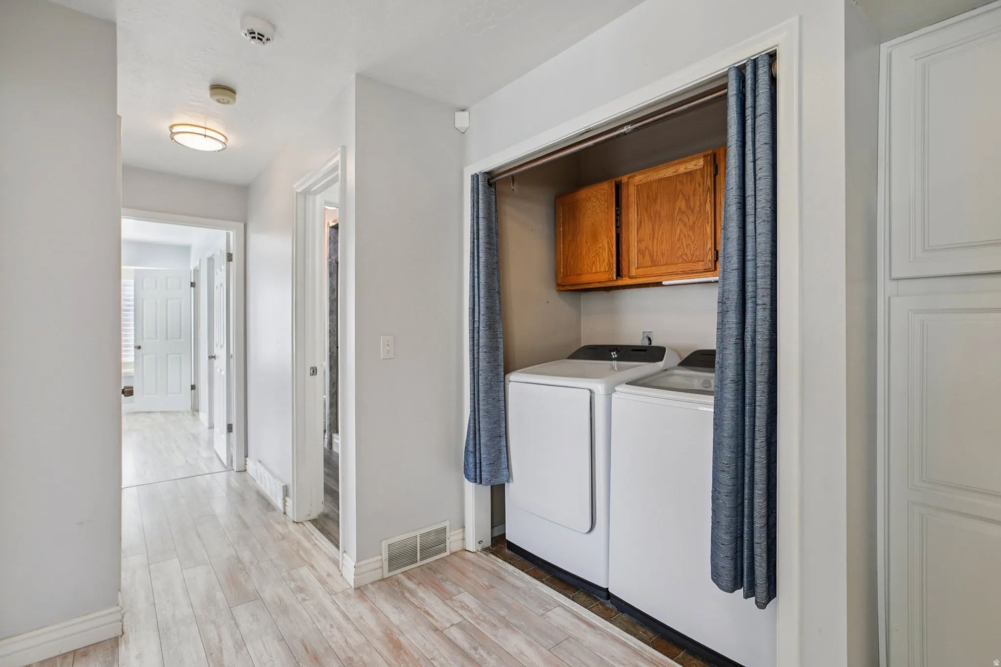 Laundry area with light wood-style floors, washing machine and clothes dryer, and cabinet space