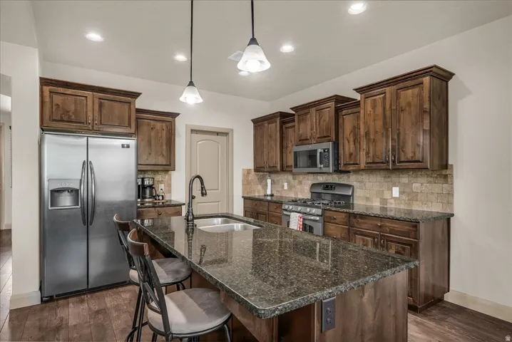 Kitchen featuring stainless steel appliances, dark stone counters, decorative backsplash, a kitchen bar, and a center island with sink