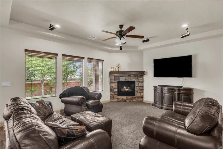 Living room with a tray ceiling, a fireplace, ceiling fan, carpet, and a textured ceiling
