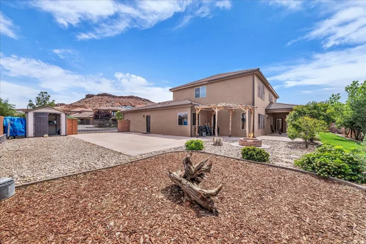 Rear view of property with a storage unit, a patio area, stucco siding, a fire pit, and a fenced backyard