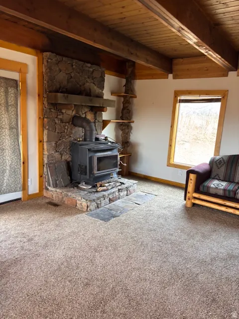 Living room featuring a wood stove, a wooden ceiling with exposed beams, and light carpet