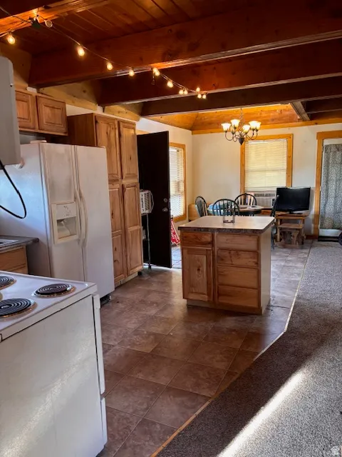 Kitchen with white appliances, dark colored carpet, dark tile patterned floors, a chandelier, and wood finish cabinets