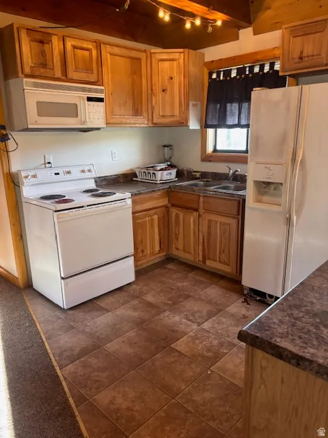 Kitchen with dark countertops, white appliances, wood finish cabinets, and track lighting
