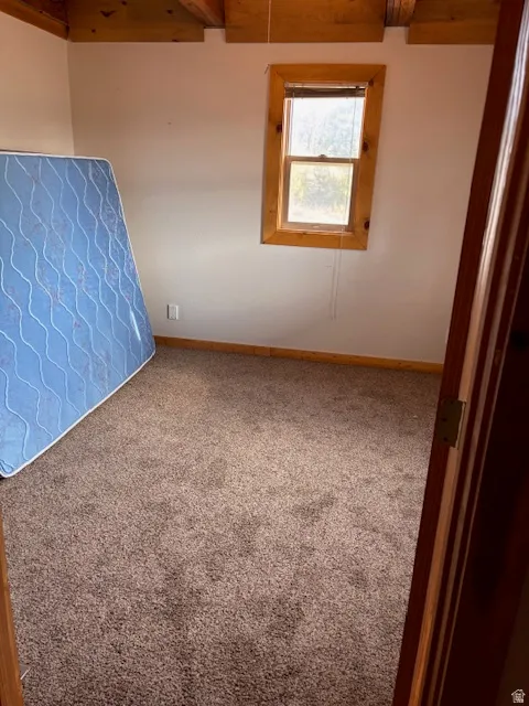 Unfurnished room with beam ceiling and carpet flooring