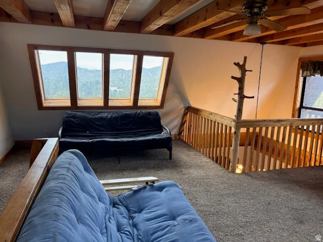 Living area featuring carpet floors, ceiling fan, beamed ceiling, and healthy amount of natural light