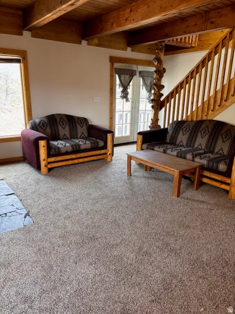 Living area with a wooden ceiling with exposed beams, light colored carpet, and french doors