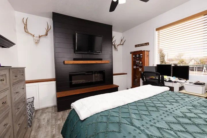 Bedroom featuring a fireplace, light wood-type flooring, a ceiling fan, and a desk