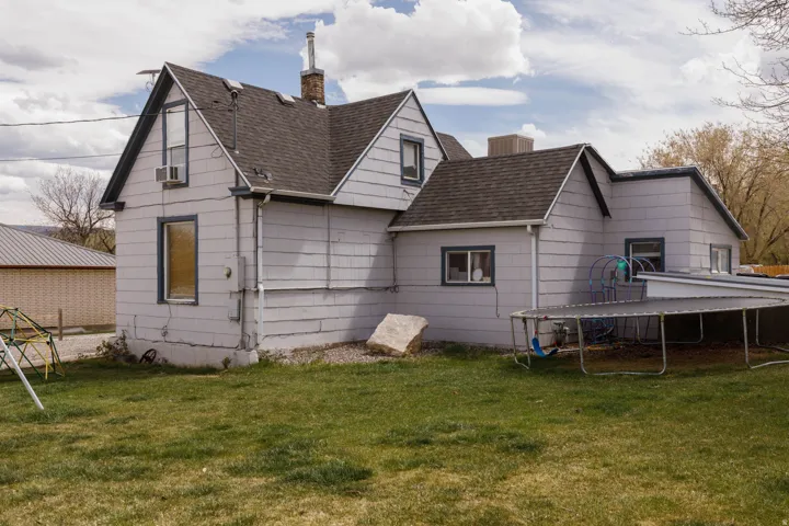 Back of house featuring a chimney, a lawn, a trampoline, and a shingled roof