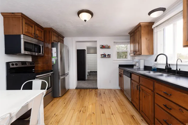 Kitchen with stainless steel appliances, light wood finished floors, wood finish cabinetry, and dark stone counters
