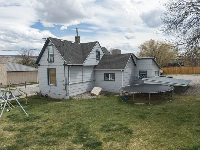 Rear view of house with a trampoline, a chimney, and roof with shingles
