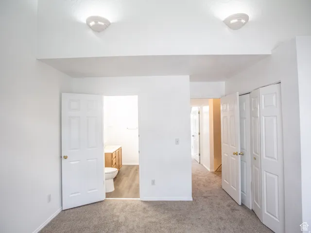 Unfurnished bedroom with light colored carpet, a closet, and ensuite bathroom