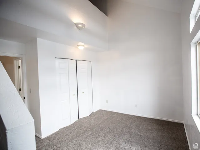 Unfurnished bedroom with dark carpet, a closet, and a high ceiling