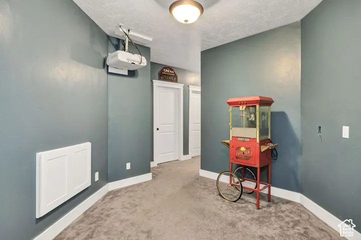 Media room featuring a ceiling-mounted projector, wall-mounted heating unit, and carpeted flooring