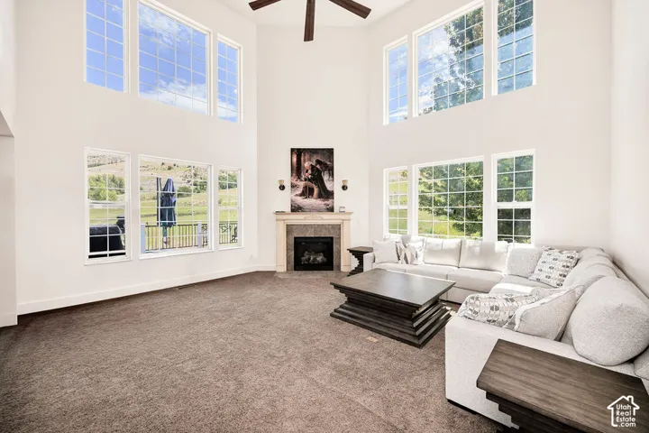 Spacious living area featuring a vaulted ceiling, abundant natural light through multiple windows, a ceiling fan, and a stone-faced fireplace with a mantel