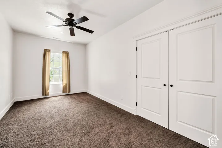 Bedroom featuring plush brown carpeting, a window with natural light, a ceiling fan with integrated lighting, and white bi-fold closet doors with black hardware