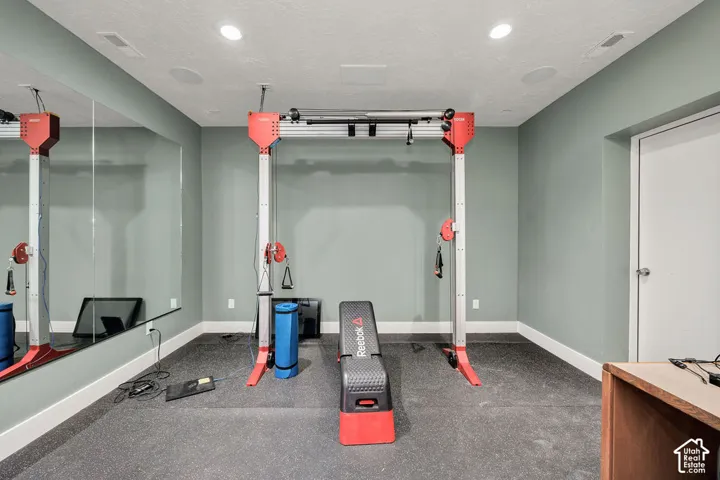 Dedicated exercise space featuring rubber flooring, a full-wall mirror, recessed lighting, and wall-mounted speakers