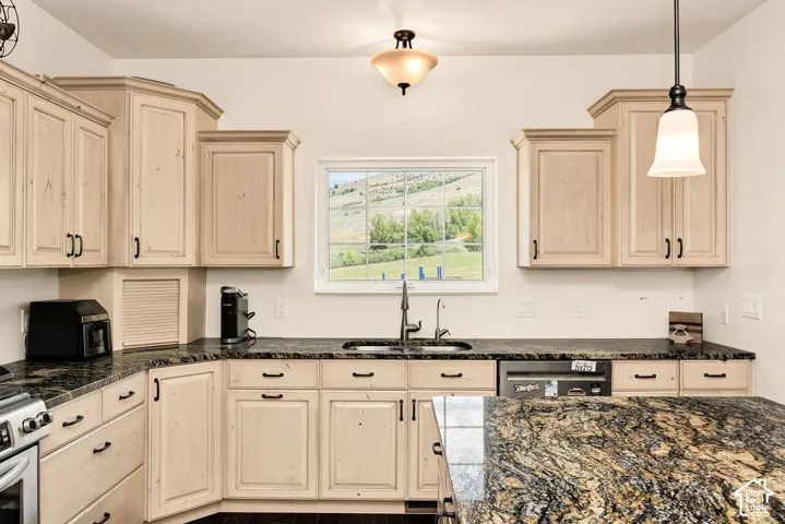 Kitchen featuring light wood-finish cabinetry, dark countertops, a built-in sink with a gooseneck faucet, and stainless steel appliances