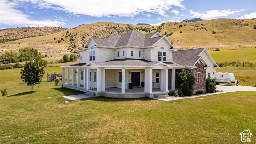Two-story residence featuring a broad wrap-around porch with white columns, a neutral-toned siding exterior, and stone accents