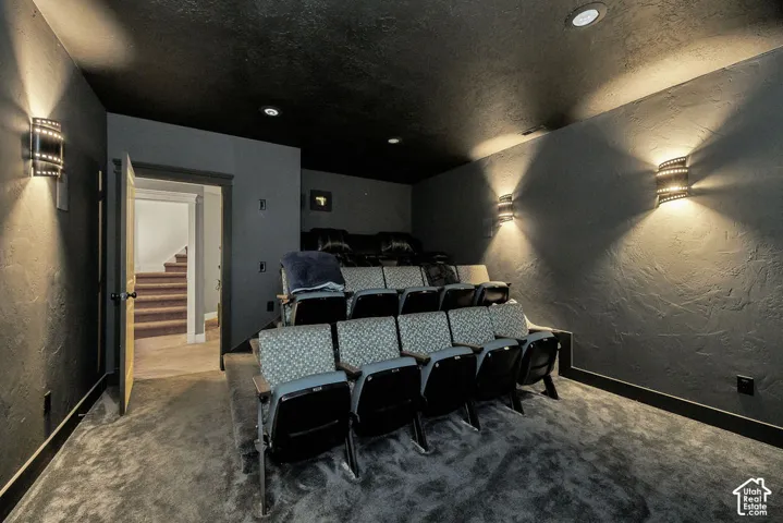 Dedicated home theater featuring tiered seating, recessed ceiling lighting, wall-mounted sconces, textured walls, and dark carpeting