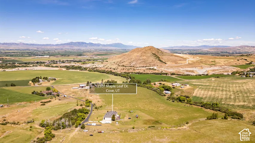 Expansive rural landscape featuring a single-family residence, surrounding green fields, and distant mountain ranges