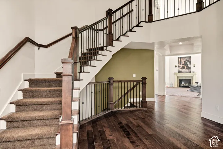 Grand entry featuring dark wood-finish flooring, a carpeted staircase with dark wood newel posts, and wrought iron balusters