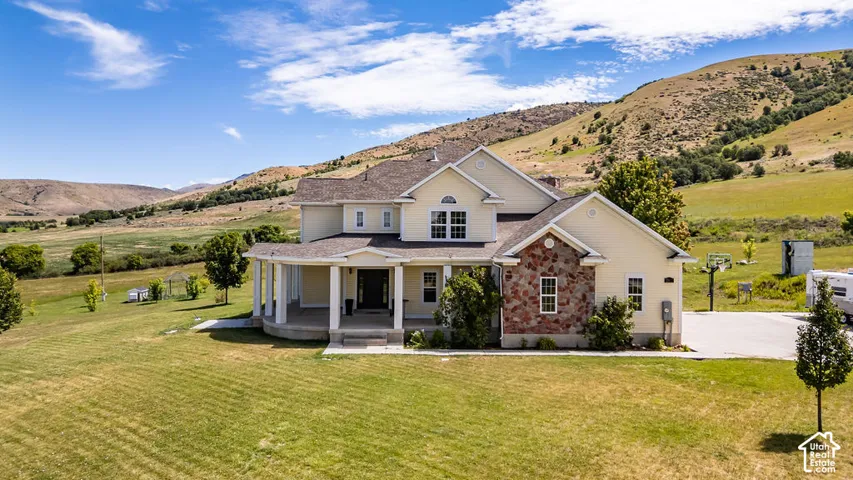 Expansive two-story residence featuring a porch with white columns, light-colored siding, and stone accents