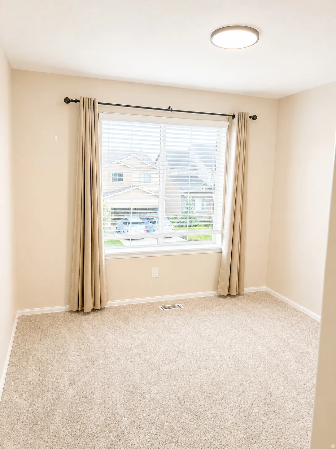 Spacious room featuring neutral carpeting, a large window with blinds, and a flush-mount ceiling light fixture