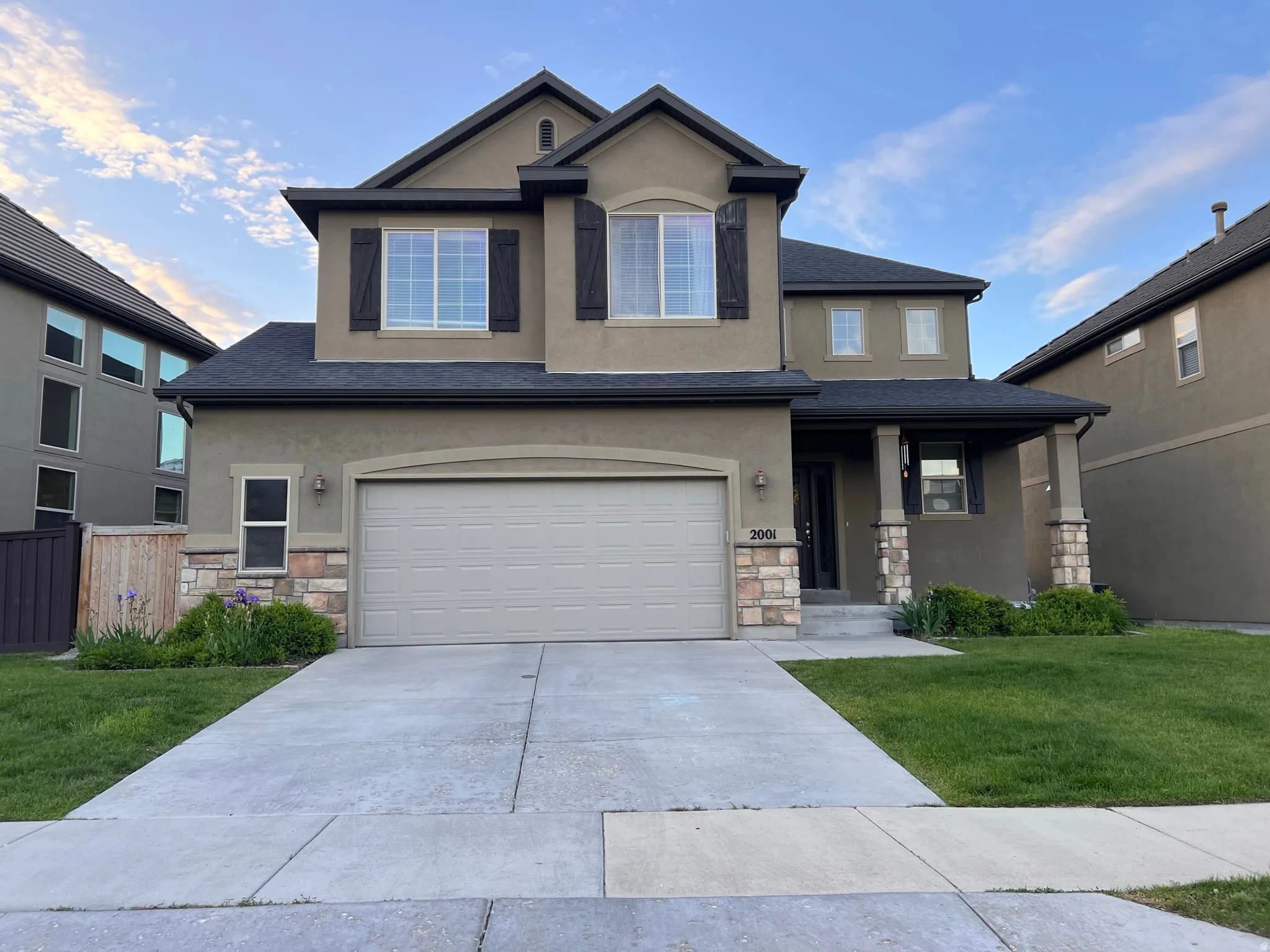 View of front facade featuring stone siding, a front yard, stucco siding, covered porch, and concrete driveway