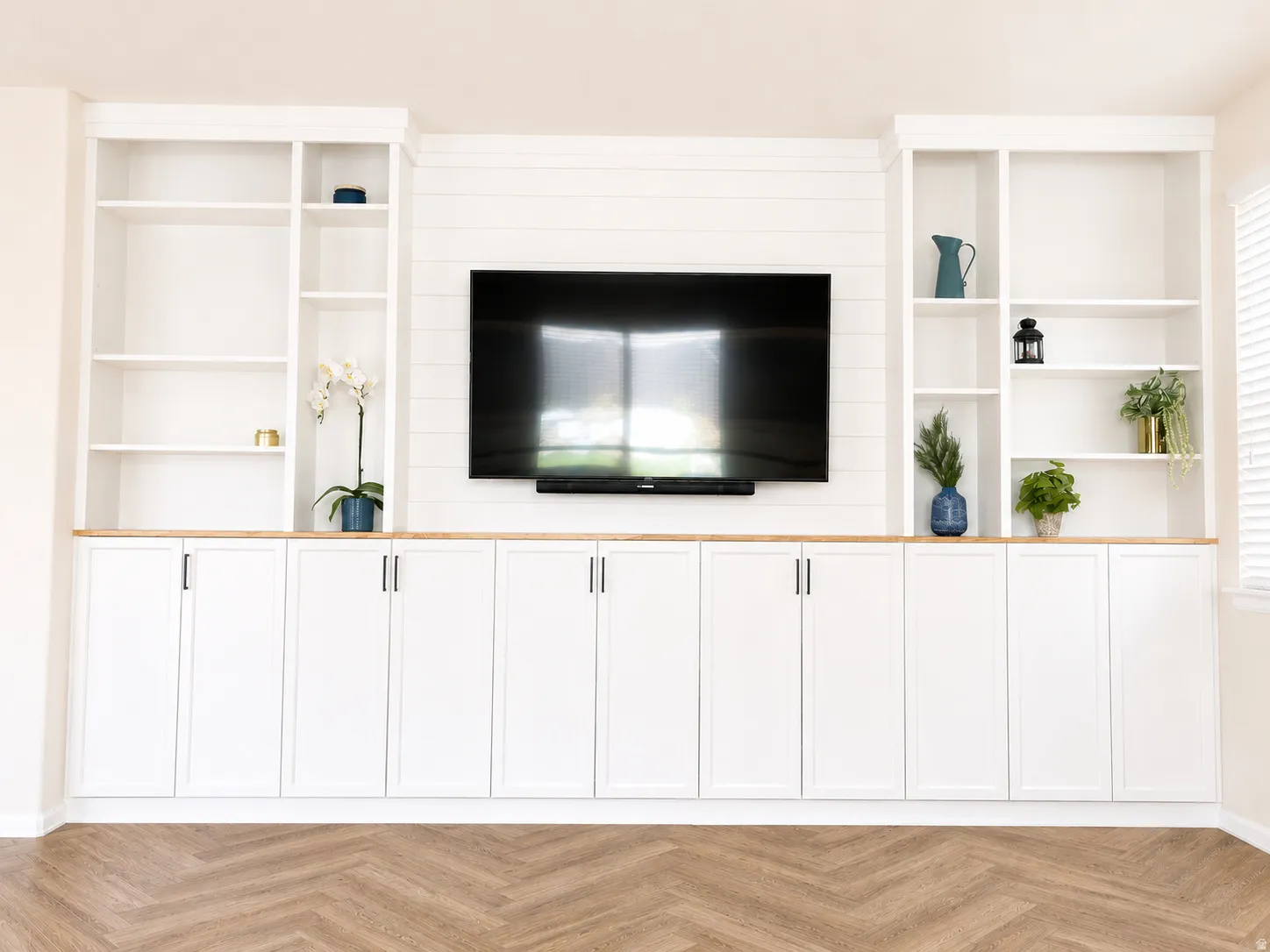 Built-in entertainment center featuring white shaker-style cabinetry, open shelving, wood-finish countertops, and shiplap wall accent