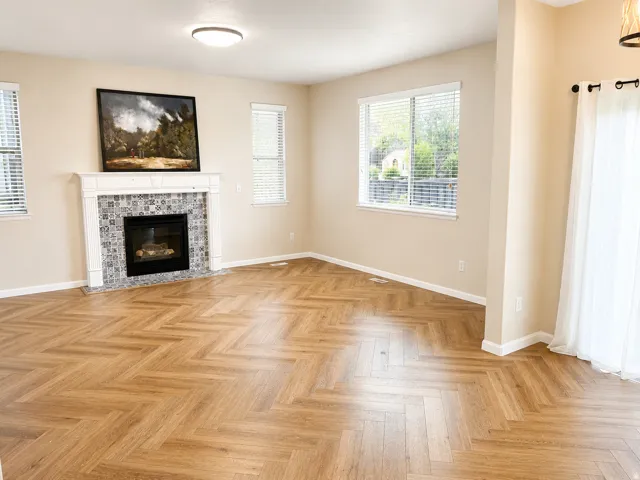 Herringbone wood-finish flooring complements a gas fireplace with a tiled surround and white mantel