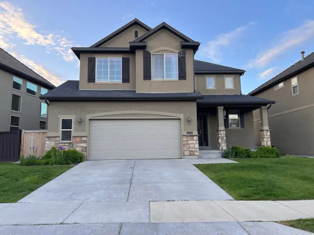 View of front of property featuring stone siding, a front yard, stucco siding, driveway, and covered porch