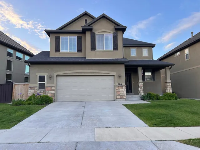 View of front facade featuring stone siding, a front yard, stucco siding, covered porch, and concrete driveway