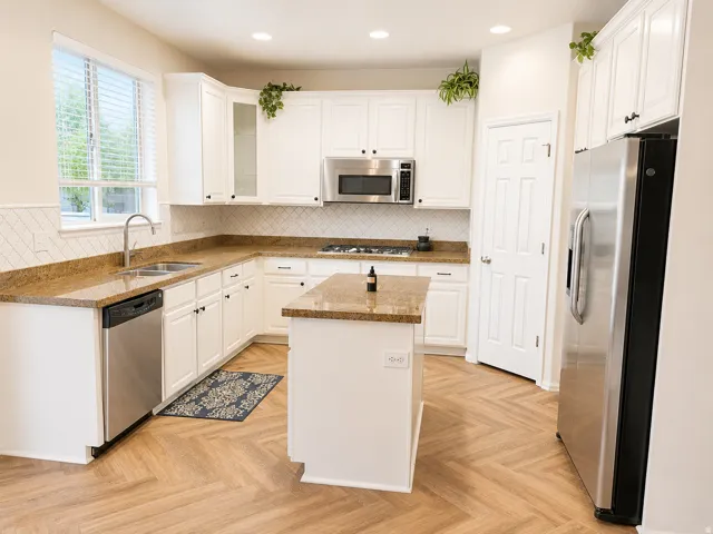 Kitchen featuring wood-finish herringbone flooring, white cabinetry, L-shaped countertops, stainless steel appliances, and a central island