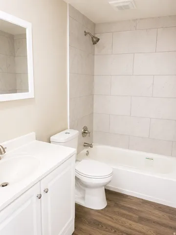 Bathroom featuring a white vanity with integrated sink, brushed nickel faucet, a white toilet, and a bathtub with a tiled shower surround
