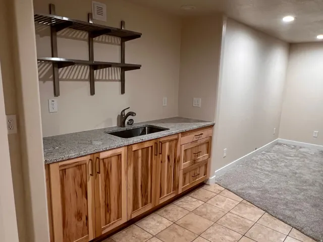 Kitchen featuring light stone countertops, recessed lighting, light tile patterned floors, light carpet, and wood finish cabinets