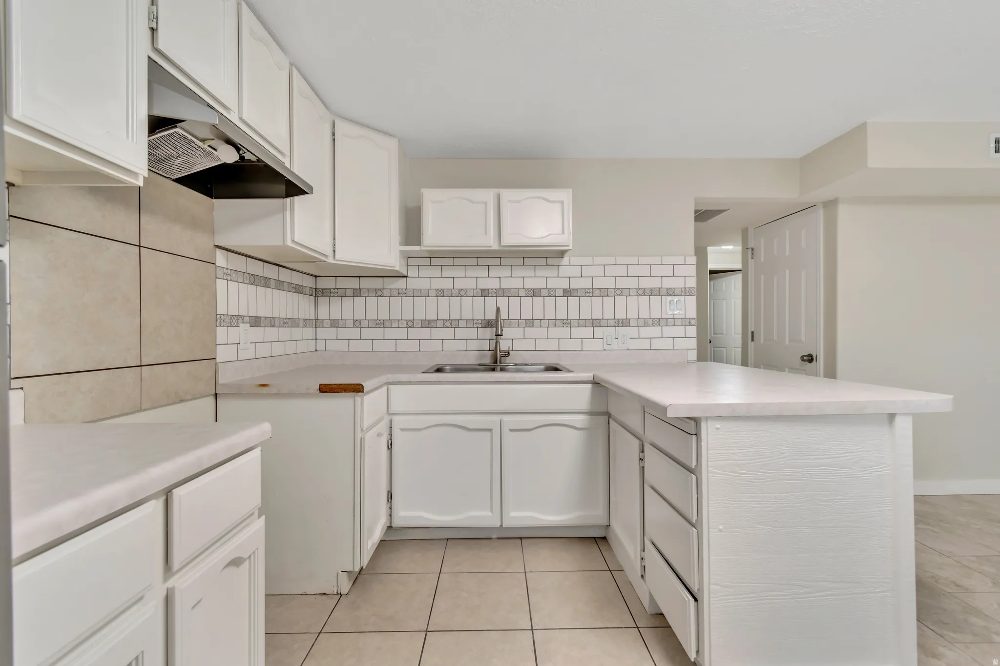 Kitchen featuring a peninsula, light countertops, white cabinetry, and tasteful backsplash